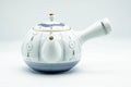 Side view of the white Arita teapot showing the spout and painted chrysanthemum-and-stripe decoration
