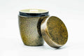 Rounded tea canister in a black-and-gold speckled finish, with the outer lid removed and leaning against the body.