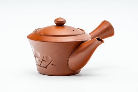 Three-quarter view of the red clay teapot, lid on, side handle to the right, with a floral band engraved on the body.