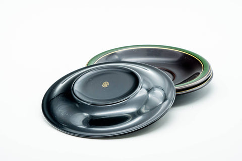 Saucers stacked at an angle, highlighting the green rim against the black lacquer.