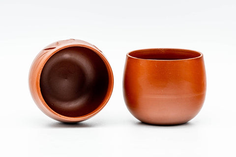 Teapot beside one yunomi teacup, showing the dark glazed cup interior