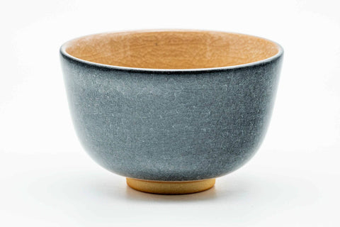 Side profile of the grey celadon chawan showing a decorative floral-and-kanji roundel and the beige glazed interior.