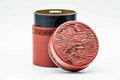 Red lacquer chazutsu tea canister, showing the carved village landscape relief on its lid