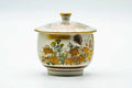 Cream Kutani-yaki lidded yunomi teacup with a gold-and-orange floral band, lid on, front view.