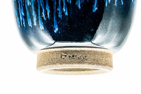 Low-angle view of one blue cup showing the unglazed foot ring and a stamped seal on the base.