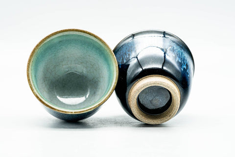 Two blue cups, one upright showing the pale glazed interior, the other on its side revealing the exposed foot and underside.