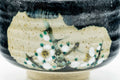 Front view of the black chawan showing the painted white floral motif on the beige reserve