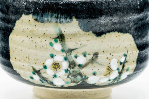 Front view of the black chawan showing the painted white floral motif on the beige reserve