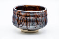 Three-quarter front view of the matcha bowl with its metallic glaze and brown drip glaze running down the sides