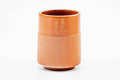 Cylindrical red shudei clay teacup with a smooth upper body bearing gold kanji and a ridged lower body, front view.