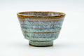 Flared teacup with a blue-grey hare's-fur streaked glaze and an amber rim, front view.