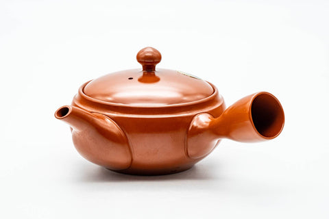 Slightly elevated view showing the domed ceramic lid and its knob on the brick-red body.