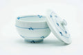Blue-and-white Arita-yaki teacup with its lid leaning beside it, showing the blue sprig motifs.
