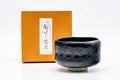 Black Kuro-raku matcha bowl shown beside its wooden tomobako box