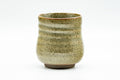 Side view of the beige speckled yunomi, highlighting the ribbed body and mottled cream-and-brown glaze.