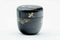 Black-lacquer matcha tea caddy with gold soaring-bird maki-e, lid on, three-quarter view showing the bird motifs on the body