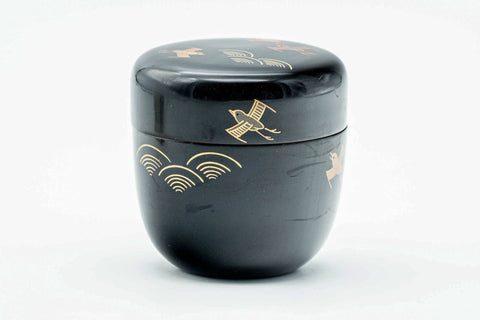 Black-lacquer matcha tea caddy with gold soaring-bird maki-e, lid on, three-quarter view showing the bird motifs on the body