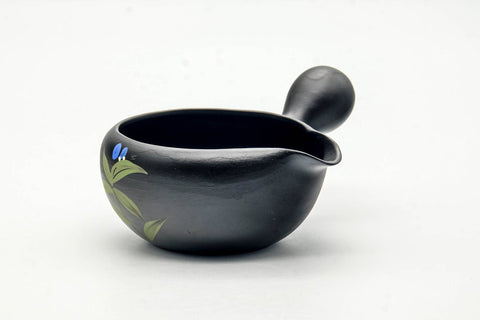 Three-quarter view of the black clay yuzamashi showing the side handle and painted leaves.