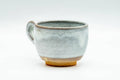 Milky-white glazed handled yunomi (ushirode), front three-quarter view with the loop handle to the right and exposed reddish clay at the foot.