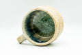 Overhead view looking straight down into the cup, the interior pooled with mottled cerulean and teal glaze, handle to one side.