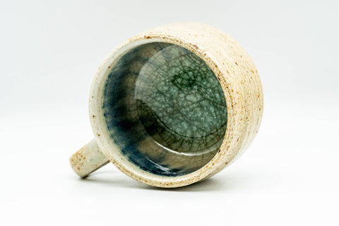 Overhead view looking straight down into the cup, the interior pooled with mottled cerulean and teal glaze, handle to one side.