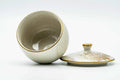 The cup with its lid propped to one side, tilted to show the glazed interior.