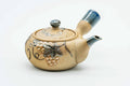 Beige side-handle kyusu painted with a blue grapevine motif and blue-tipped spout, lid on, three-quarter view.