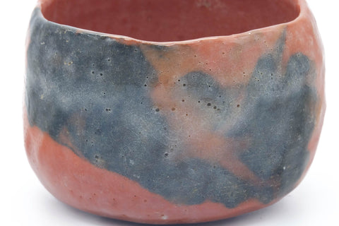 Three-quarter view emphasizing the patchy grey-and-red surface of the handbuilt raku bowl.
