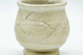 Close-up of the larger cream-glazed cup showing its incised surface design.