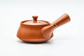 Side profile of the teapot with the hollow handle to the right and spout to the left.