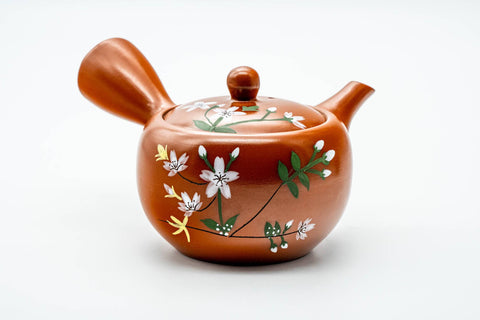 Three-quarter front view of a red shudei Tokoname-yaki kyusu teapot hand-painted with white floral sprays, lid on, side handle at right and spout at left.
