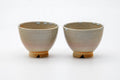 A pair of pale-glazed Hagi-yaki yunomi set side by side on a white background.