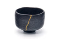 Black kuro-raku matcha bowl with a gold kintsugi repair line, front view.