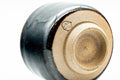 Low-angle view of one black cup showing the foot ring and a stamped seal on the base.