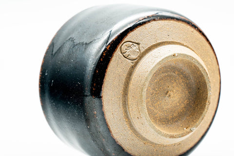 Low-angle view of one black cup showing the foot ring and a stamped seal on the base.