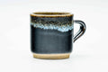 Dark blue-black handled yunomi (ushirode) with a pale hare's-fur drip rim, front view with the handle to the right.