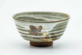 Matcha bowl with a grey-and-white drip glaze and spiraling horizontal ridges, accented with a small painted floral motif, front view.