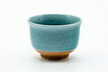 Yunomi in a turquoise-blue celadon glaze with an unglazed clay foot, front view.