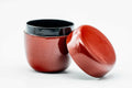 Glossy red-brown urushi-lacquer matcha tea caddy with the lid removed, the body revealing a dark interior and the lid resting beside it.