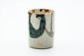 Cylindrical Mino-yaki yunomi in white Shino glaze with abstract green-and-brown brushwork, front view.