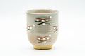 Beige yunomi teacup, front view, decorated with small scattered floral sprigs in red, green and blue over a ribbed body.