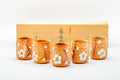 Set of five orange Shino-glazed yunomi teacups arranged in their wooden box, each painted with white plum blossoms.