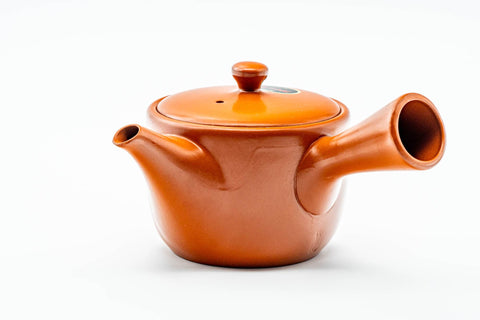 Side profile of the red clay teapot, spout to the left and hollow side handle facing the viewer.