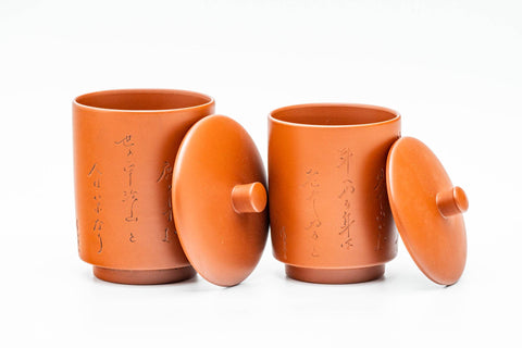 The two lidded cups with lids lifted off and leaning against them, showing the engraved calligraphy on the bodies.