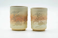 Pair of cylindrical Hagi-yaki teacups, one larger and one smaller, with a beige-pink glaze, spiraling ridges, and engraved florals, shown side by side.