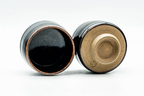 Two black cups, one upright showing the glossy black interior, the other on its side revealing the exposed foot.