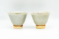 The matching pair of beige Hagi-yaki cups, front view showing the conical form and exposed buff clay foot.