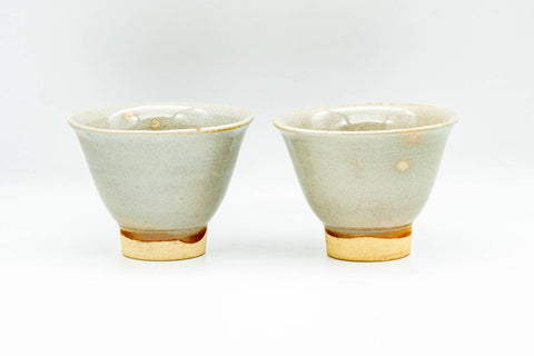 The matching pair of beige Hagi-yaki cups, front view showing the conical form and exposed buff clay foot.