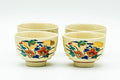 Set of beige Kutani-yaki teacups grouped together, each hand-painted with a colourful floral and bird motif in red, green and gold, shown upright on trimmed foot rings.