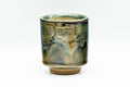 Cylindrical yunomi teacup, front view, in a brown and green drip glaze with earthy tones.